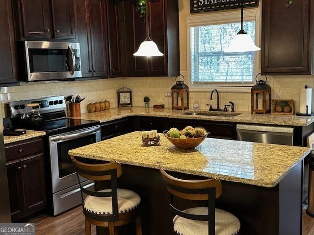 kitchen featuring stainless steel appliances, a kitchen bar, sink, and hanging light fixtures