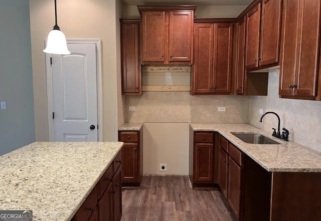 kitchen with decorative backsplash, light stone counters, dark wood-style flooring, pendant lighting, and a sink