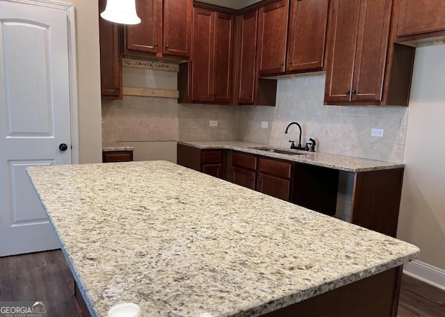 kitchen with dark wood finished floors, tasteful backsplash, a sink, a kitchen island, and baseboards