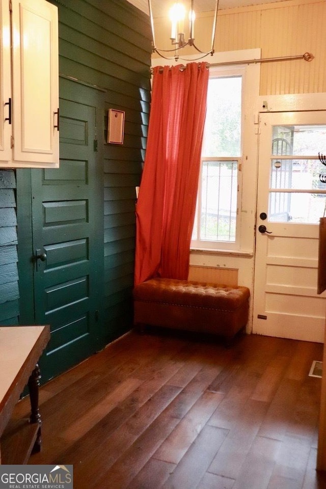 doorway featuring dark wood-type flooring, wooden walls, and a chandelier