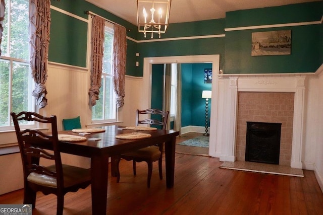 dining area with a tiled fireplace, a notable chandelier, and hardwood / wood-style flooring