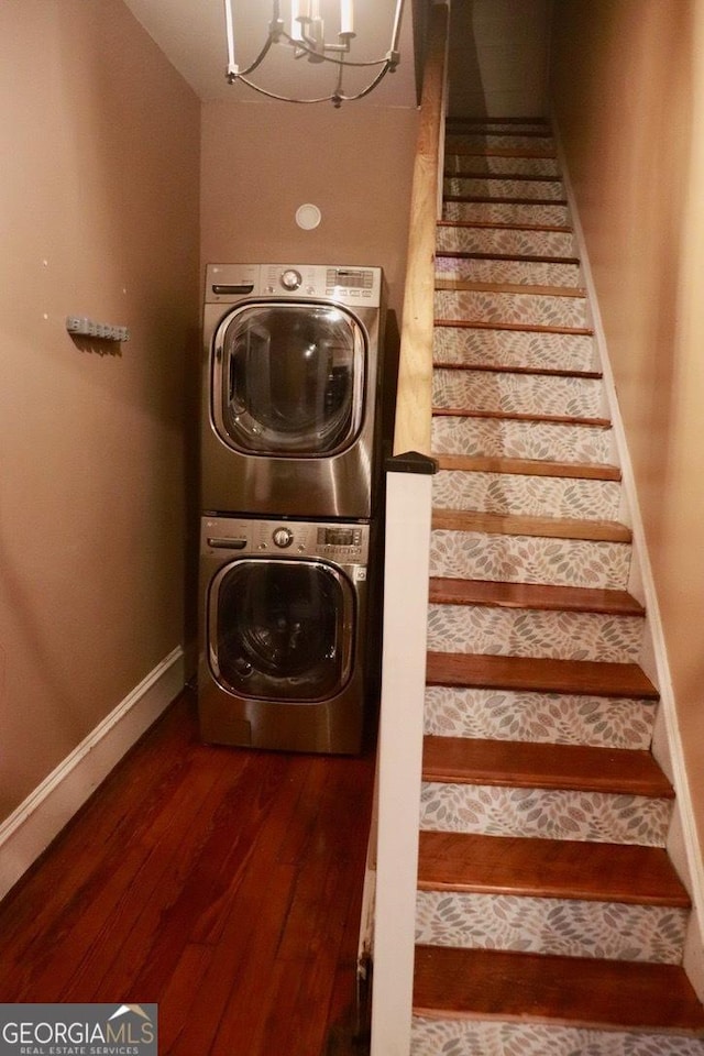 clothes washing area featuring dark hardwood / wood-style floors, stacked washer and clothes dryer, and a chandelier