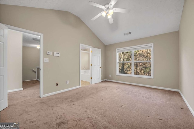 unfurnished bedroom featuring vaulted ceiling, connected bathroom, a walk in closet, light colored carpet, and ceiling fan