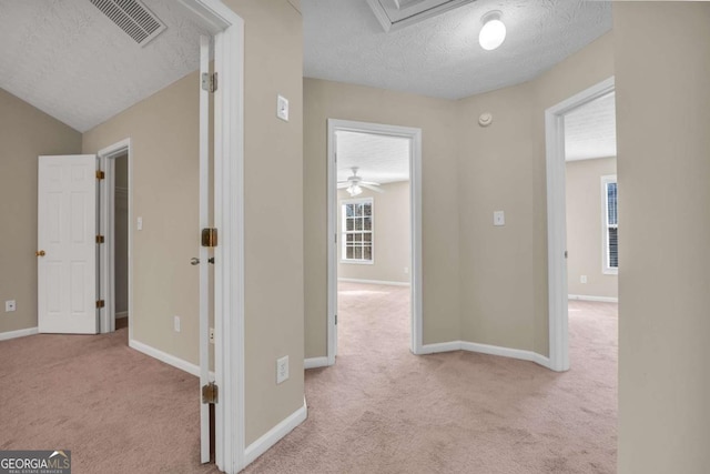 corridor featuring vaulted ceiling, light colored carpet, and a textured ceiling