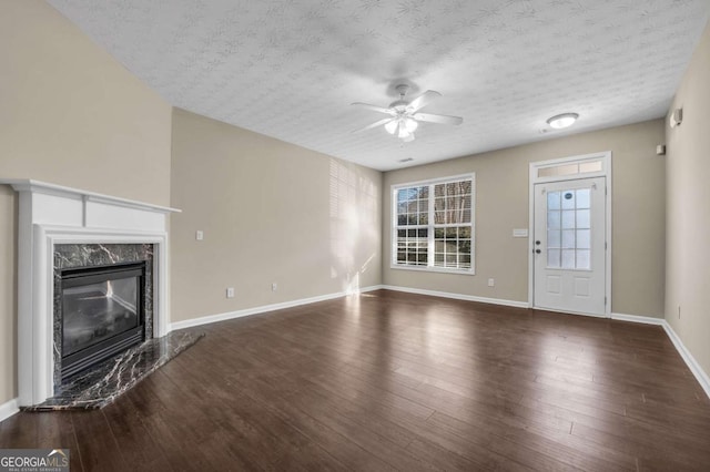 unfurnished living room featuring ceiling fan, dark wood-type flooring, a high end fireplace, and a textured ceiling