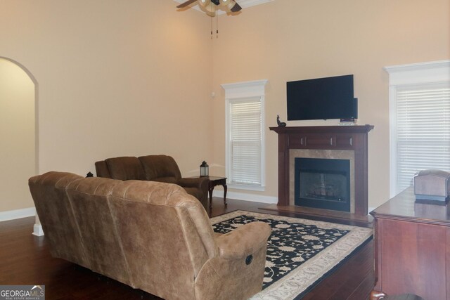 living room featuring a tiled fireplace, dark wood-type flooring, and ceiling fan