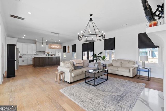 living room with an inviting chandelier, ornamental molding, and light wood-type flooring