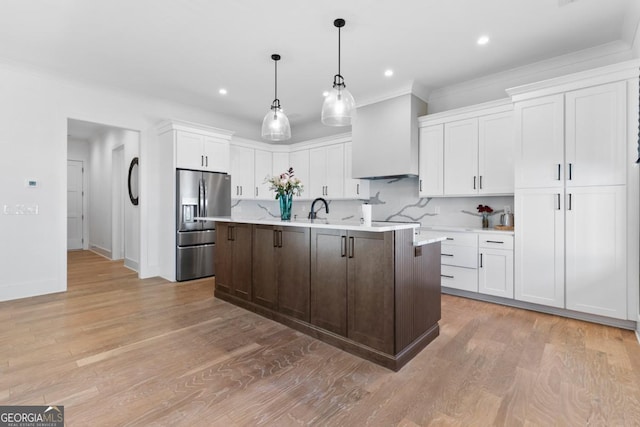 kitchen with stainless steel fridge, white cabinetry, tasteful backsplash, a center island with sink, and decorative light fixtures