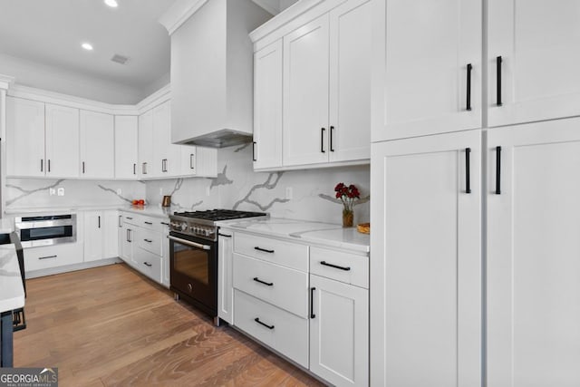 kitchen featuring white cabinetry, light hardwood / wood-style flooring, backsplash, stainless steel range with gas cooktop, and wall chimney range hood