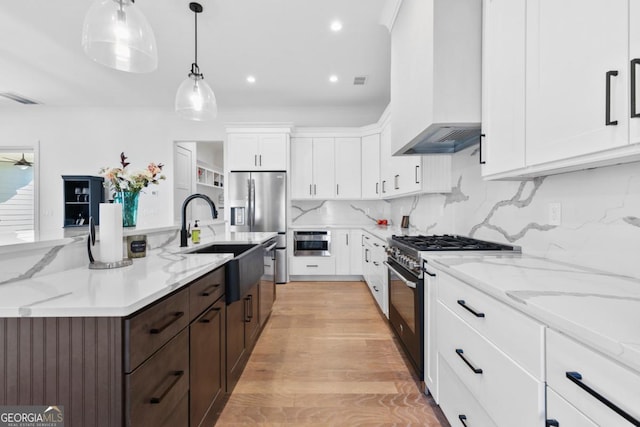 kitchen featuring pendant lighting, white cabinetry, decorative backsplash, stainless steel appliances, and wall chimney range hood