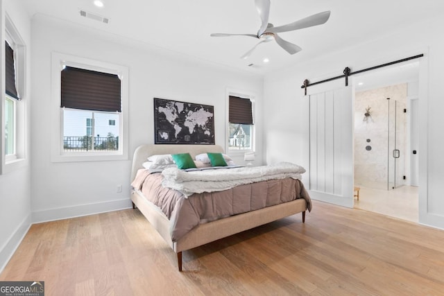 bedroom with a barn door, ceiling fan, and light hardwood / wood-style floors