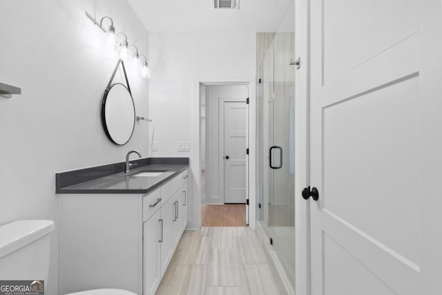 bathroom with a shower with door, vanity, and toilet