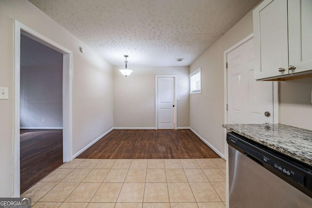 kitchen with dishwasher, white cabinets, light tile patterned floors, light stone counters, and a textured ceiling