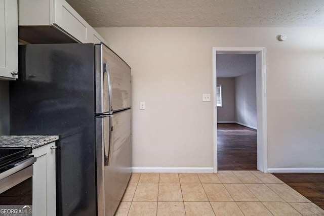 kitchen featuring stainless steel fridge, light tile patterned flooring, white cabinets, and a textured ceiling