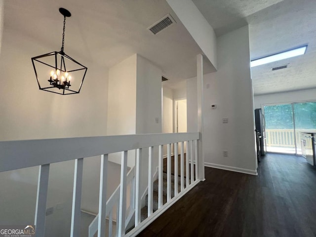 hall with dark wood-type flooring, a textured ceiling, and a chandelier