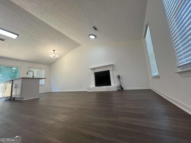 unfurnished living room featuring lofted ceiling, sink, dark wood-type flooring, a textured ceiling, and a chandelier