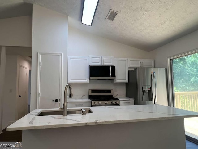 kitchen with white cabinets, vaulted ceiling, appliances with stainless steel finishes, and an island with sink