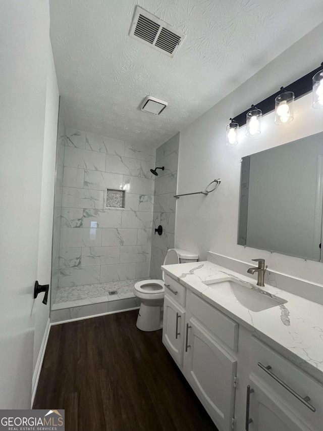 bathroom with a tile shower, wood-type flooring, vanity, toilet, and a textured ceiling