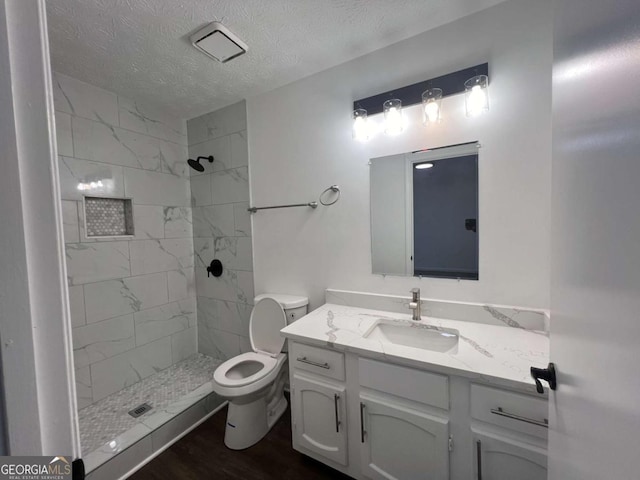 bathroom featuring toilet, a textured ceiling, a tile shower, vanity, and hardwood / wood-style flooring