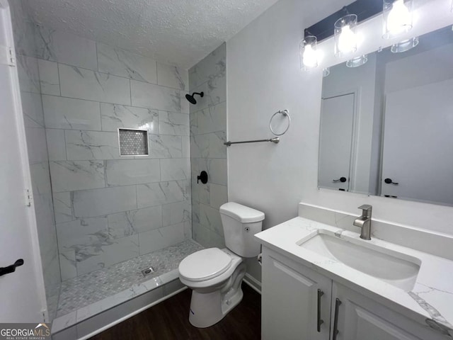 bathroom with wood-type flooring, vanity, tiled shower, toilet, and a textured ceiling