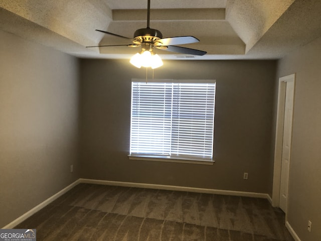 empty room with dark colored carpet, a textured ceiling, and a tray ceiling