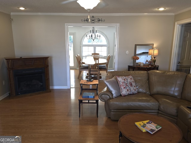 living area featuring baseboards, wood finished floors, crown molding, a fireplace, and a chandelier