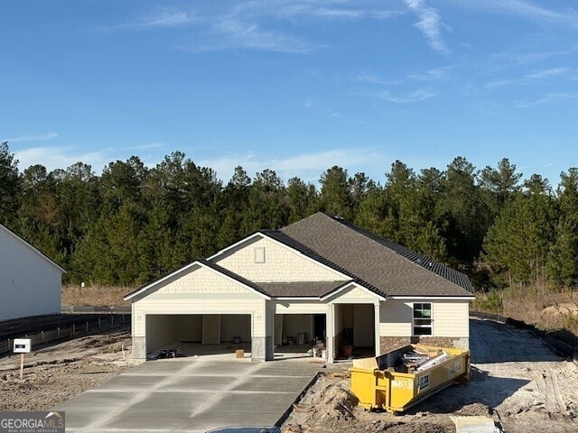 view of front facade featuring an attached garage, a view of trees, concrete driveway, and roof with shingles