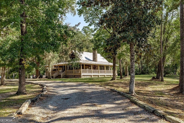 farmhouse inspired home featuring gravel driveway, covered porch, and metal roof