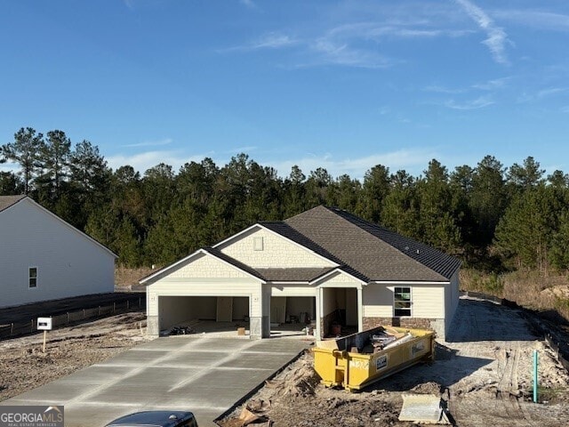 view of front facade featuring a garage, concrete driveway, a shingled roof, and a forest view