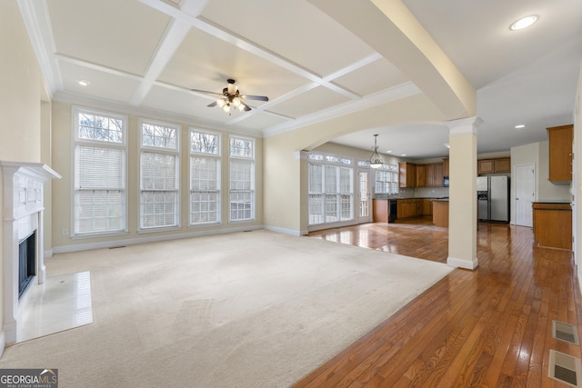 unfurnished living room featuring ornamental molding, coffered ceiling, ceiling fan with notable chandelier, and decorative columns