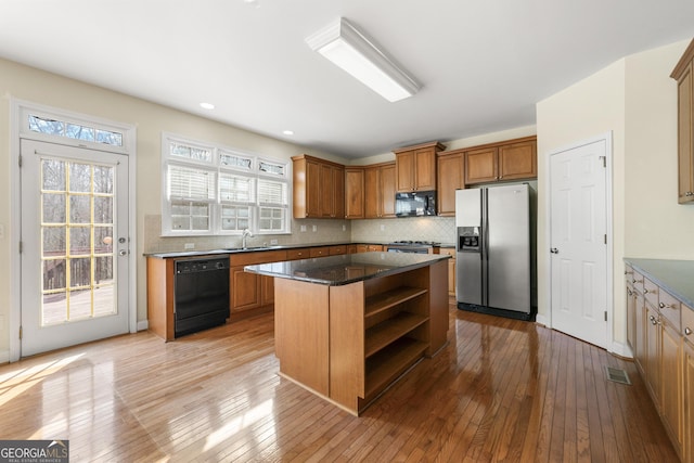 kitchen featuring sink, black appliances, a kitchen island, light hardwood / wood-style floors, and backsplash