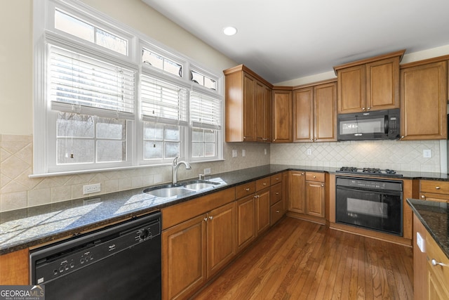 kitchen with dark stone counters, dark hardwood / wood-style flooring, sink, and black appliances