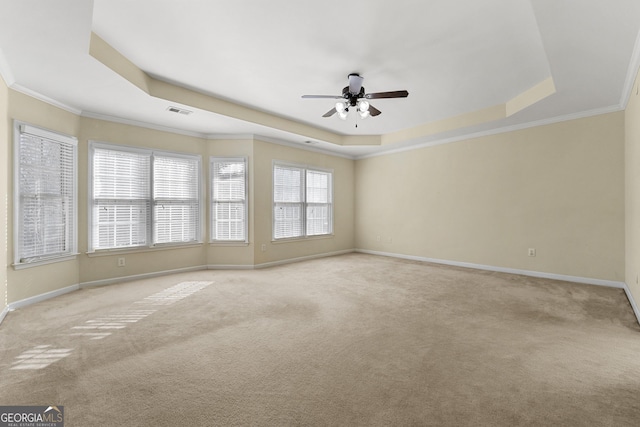 empty room with ornamental molding, a tray ceiling, and light carpet