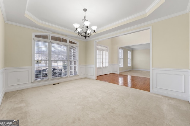 empty room with crown molding, a tray ceiling, carpet floors, and a notable chandelier