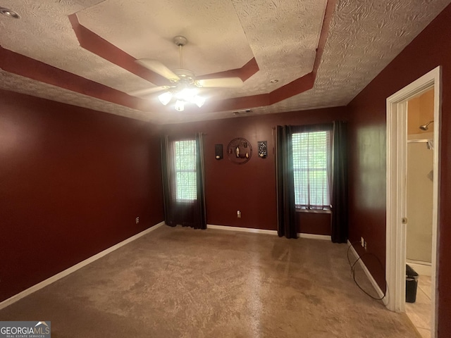 interior space with a textured ceiling, ceiling fan, a raised ceiling, and baseboards