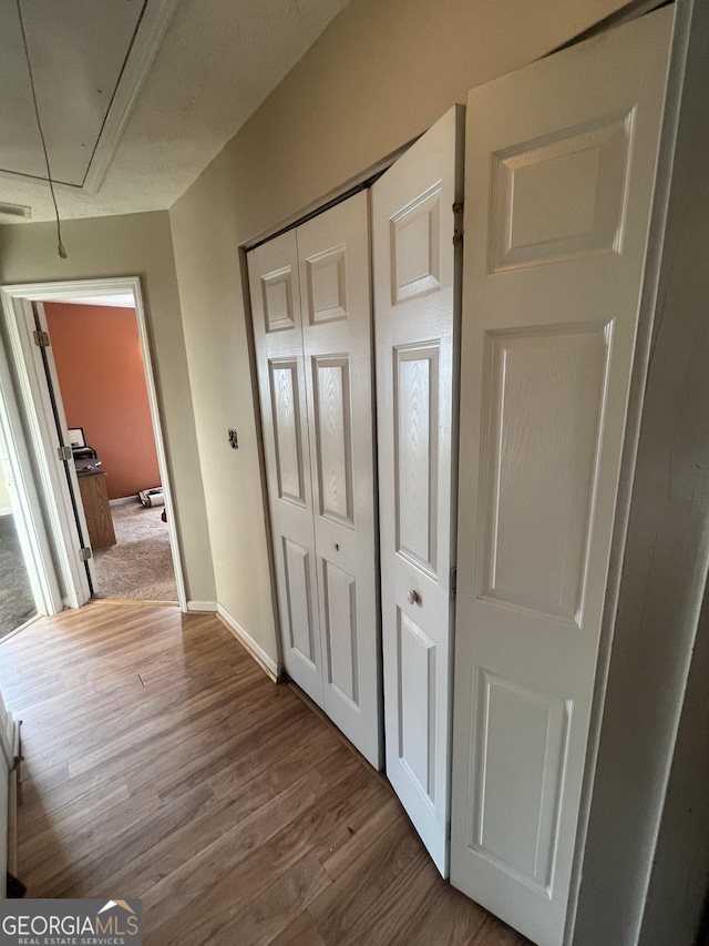 corridor featuring wood finished floors, attic access, and baseboards