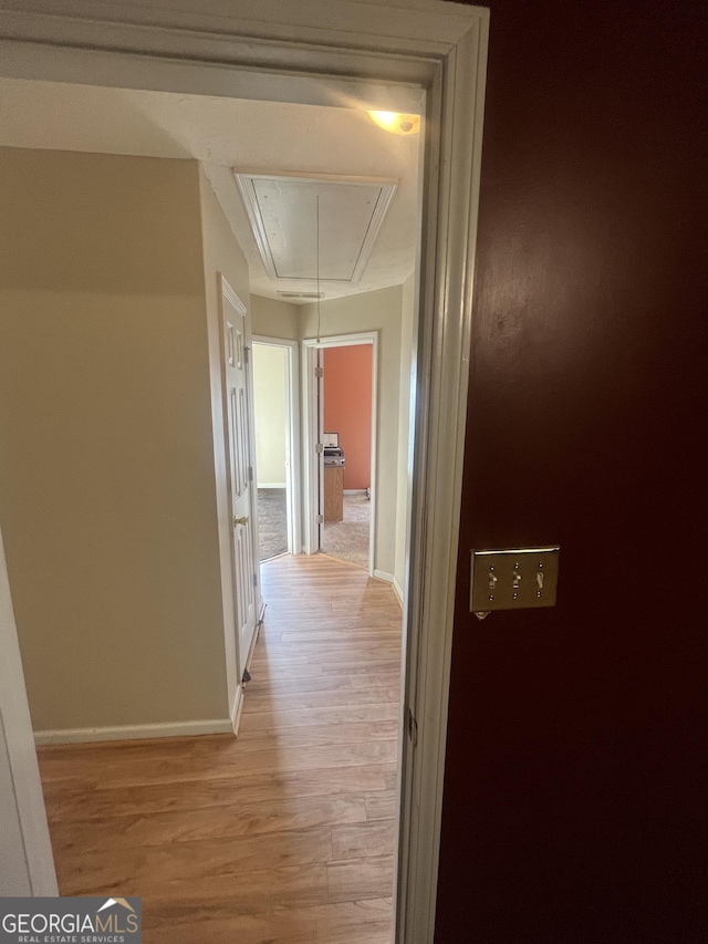 hall featuring light wood-style floors, attic access, and baseboards