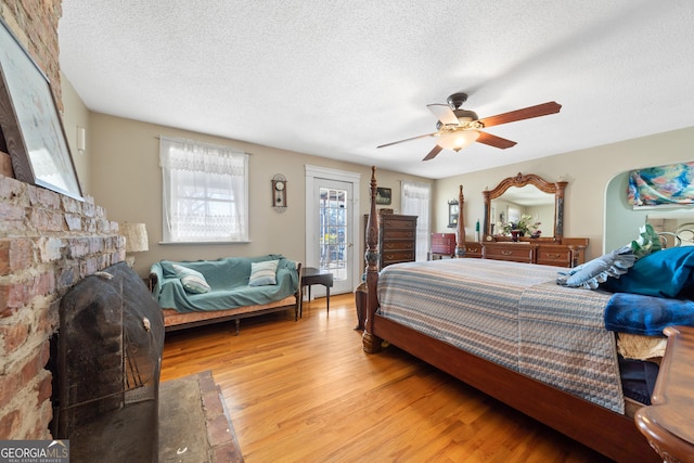 bedroom featuring light wood finished floors, ceiling fan, a fireplace, and a textured ceiling