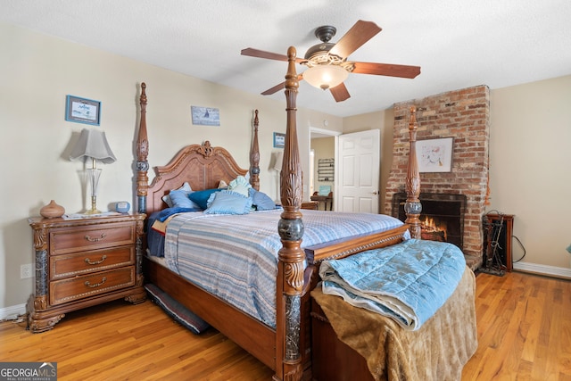 bedroom with a textured ceiling, a fireplace, a ceiling fan, baseboards, and light wood finished floors