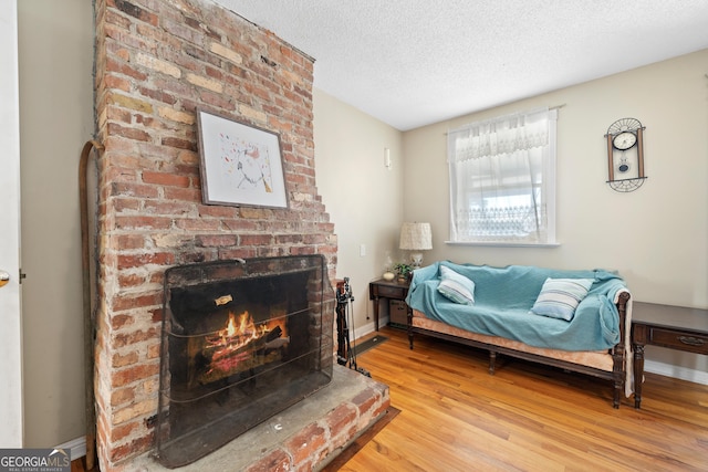 living area with a brick fireplace, baseboards, light wood finished floors, and a textured ceiling