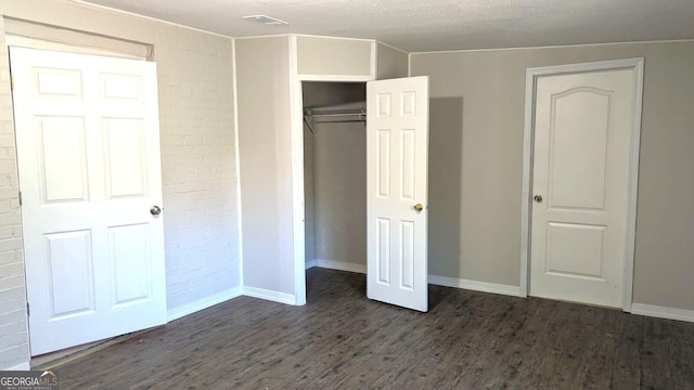 unfurnished bedroom featuring brick wall, dark wood-type flooring, a textured ceiling, and a closet