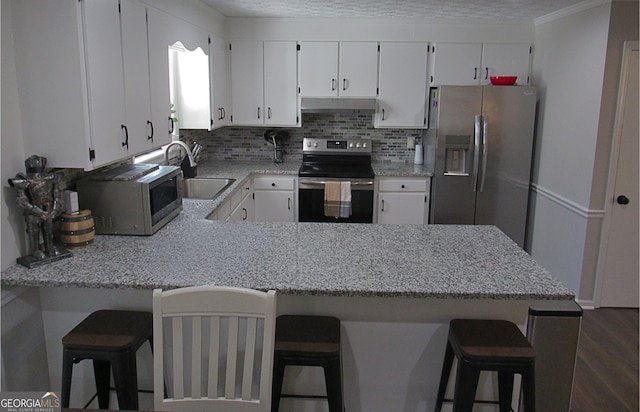 kitchen featuring stainless steel appliances, kitchen peninsula, white cabinets, and a kitchen bar