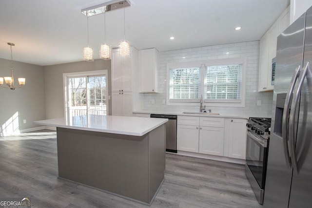 kitchen featuring sink, backsplash, hanging light fixtures, stainless steel appliances, and white cabinets