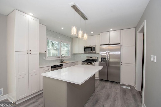 kitchen featuring sink, appliances with stainless steel finishes, white cabinetry, backsplash, and a center island