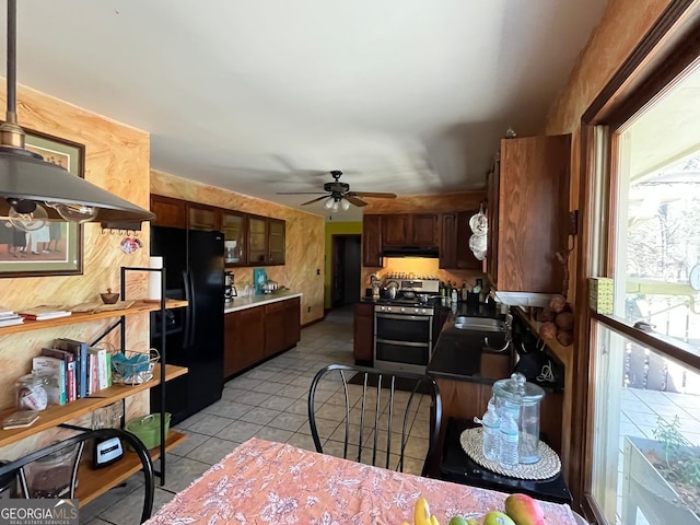 kitchen featuring sink, light tile patterned floors, stainless steel range, dark brown cabinetry, and black fridge with ice dispenser