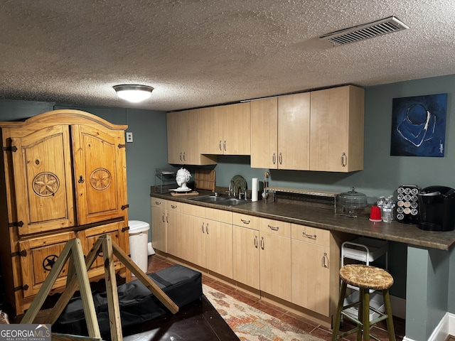 kitchen featuring a breakfast bar area, sink, a textured ceiling, and light brown cabinets