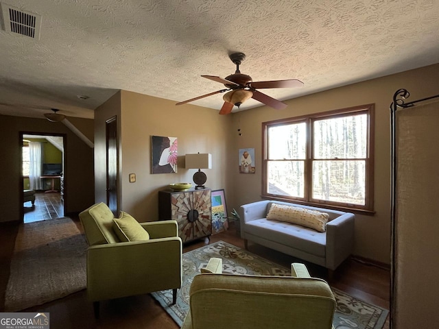 living room with dark hardwood / wood-style flooring, ceiling fan, and a textured ceiling