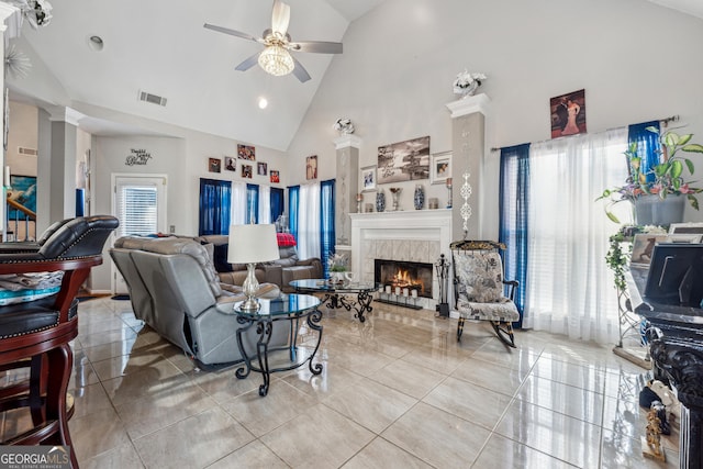 living room with ceiling fan, high vaulted ceiling, decorative columns, light tile patterned flooring, and a tiled fireplace