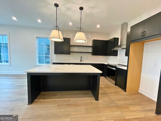 kitchen featuring wall chimney range hood, decorative light fixtures, a kitchen island, and range with electric stovetop