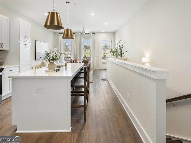 kitchen featuring a breakfast bar, hanging light fixtures, dark hardwood / wood-style flooring, an island with sink, and white cabinets